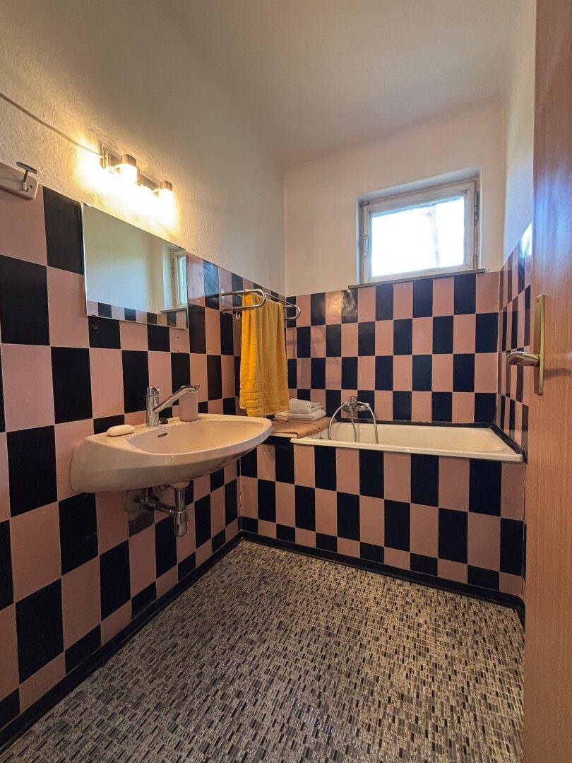 Badezimmer mit auffälligen schwarz-rosa Fliesen, Badewanne, Einzelwaschbecken und Fenster.
