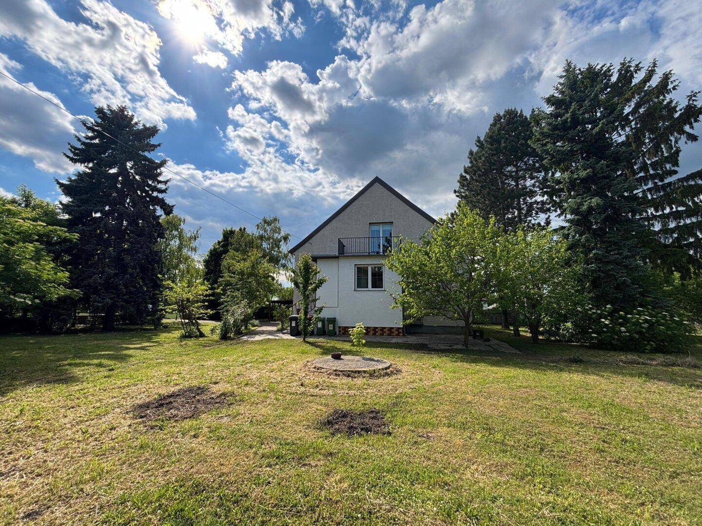 Rückseite des Hauses mit Balkon und großem, sonnigen Gartenbereich.