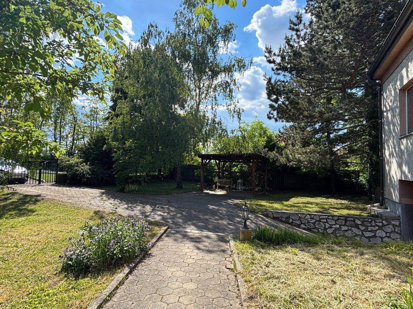 Großer Gartenbereich mit gepflastertem Weg, Pergola und viel Grün.