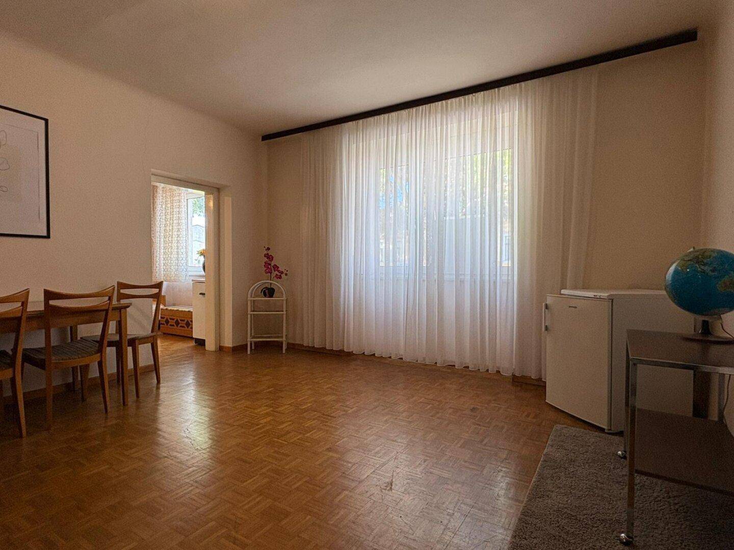 Heller Wohnbereich mit Parkettboden, großem Fenster und Esstisch für gesellige Stunden.