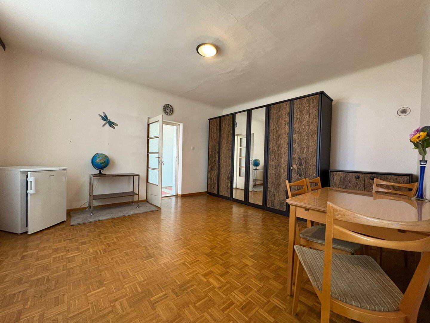 Geräumiges Schlafzimmer mit Parkettboden, Kleiderschrank und Esstisch in einfacher Einrichtung.