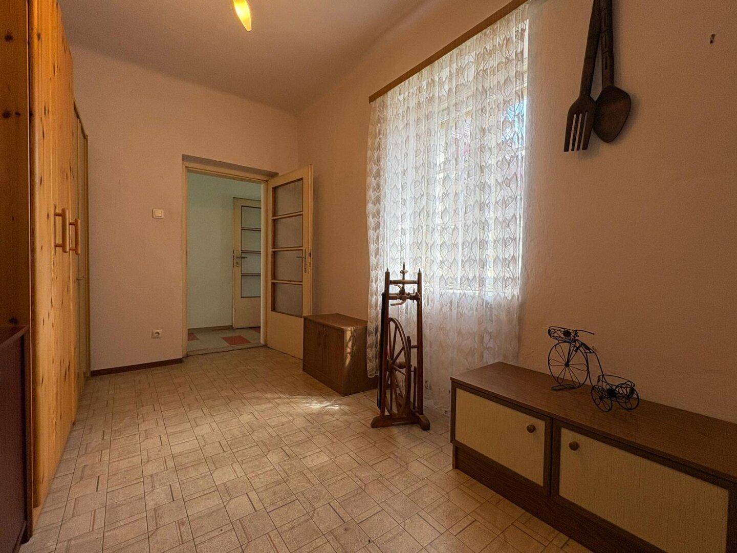 Zimmer mit Holzmöbeln, Fenster und gemustertem Bodenbelag, ideal als Arbeits- oder Gästezimmer.