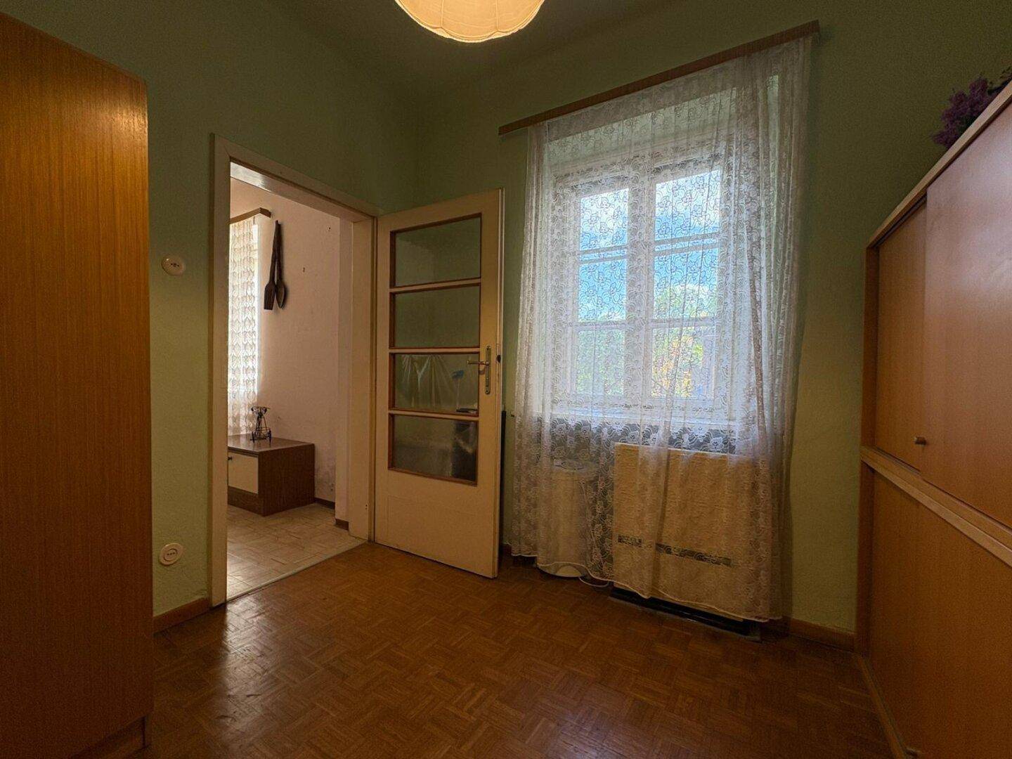 Zimmer mit grünen Wänden, Parkettboden und Fenster mit Vorhängen, bietet eine ruhige Atmosphäre.
