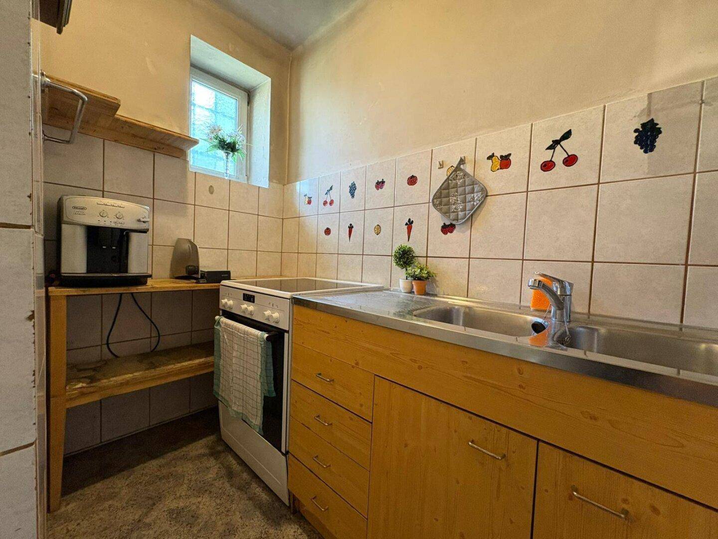 Einfache Küche mit Holzschränken, Spüle und Herd, dekoriert mit Fliesen und Fenster.