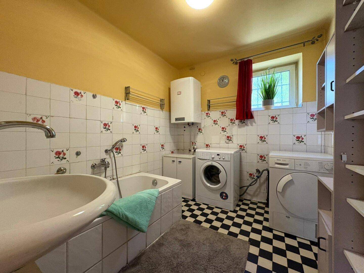 Badezimmer mit Badewanne, Waschmaschine und Trockner, gefliestem Boden und Wänden.