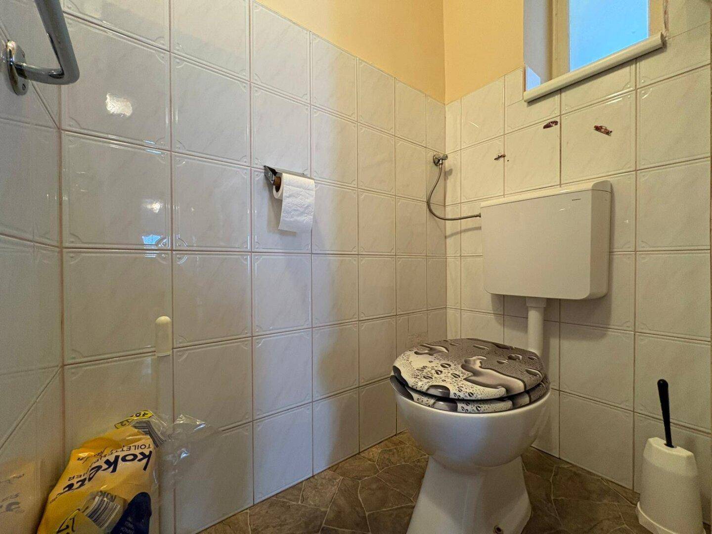 Separate Toilette mit Fliesenwänden und Fenster, praktisch und funktional.