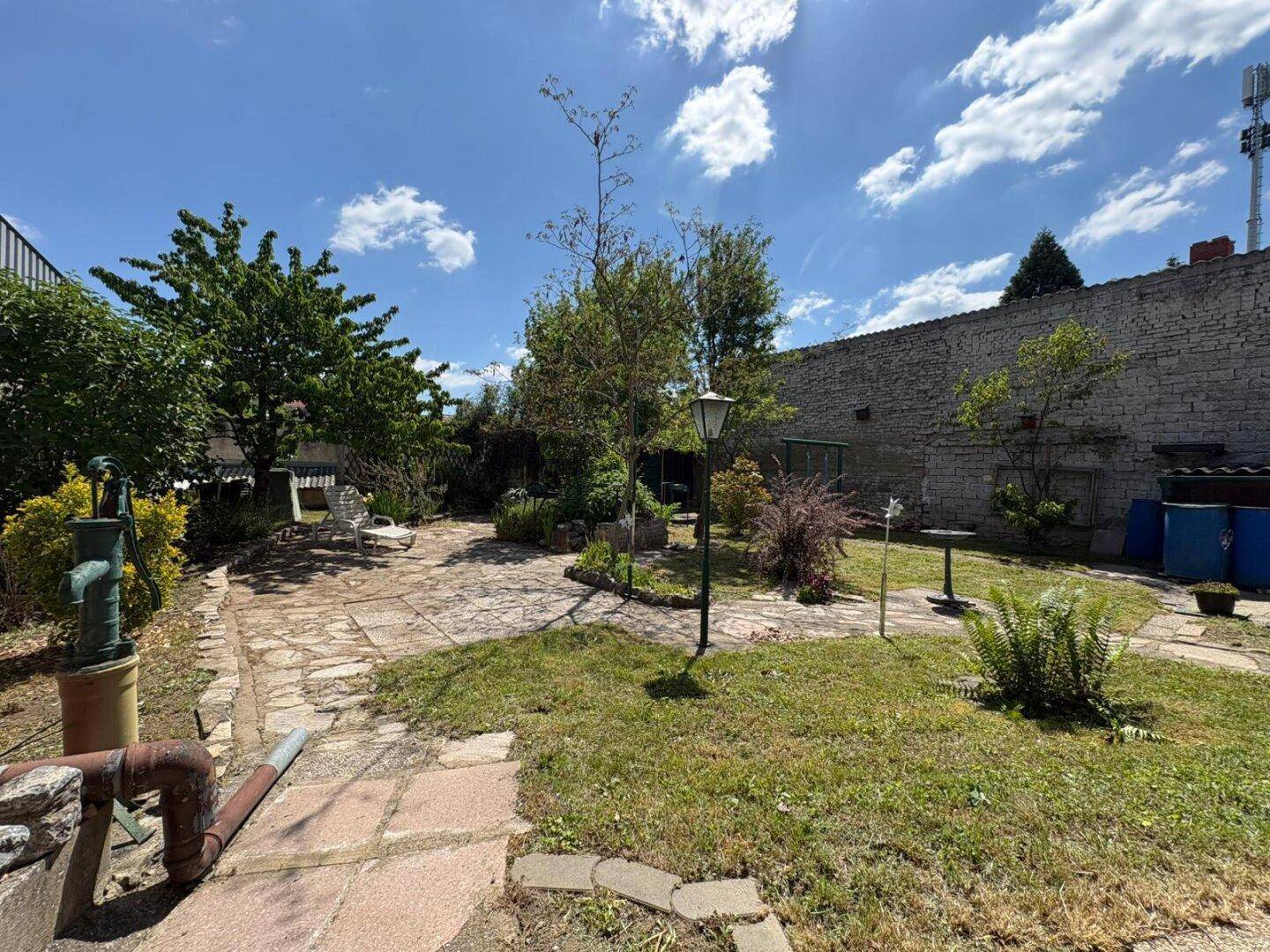 Großer Gartenbereich mit Steinplattenweg, Rasenflächen und alten Bäumen unter blauem Himmel.