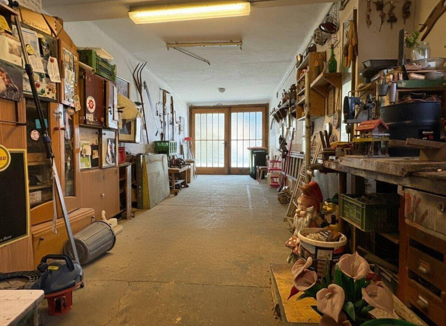 Langer, schmaler Werkstattraum mit Regalen voller Werkzeuge und Materialien, hell beleuchtet.