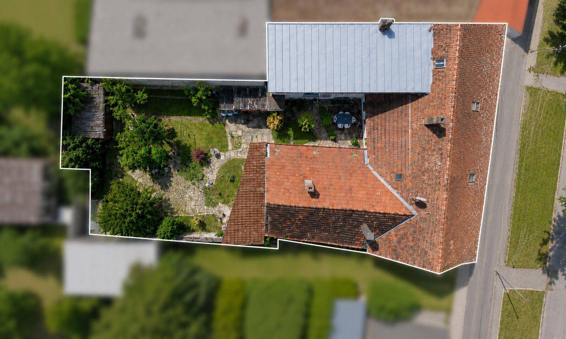 Luftaufnahme eines Anwesens mit Wohnhaus, Garten und Grundstücksgrenzen unter blauem Himmel.