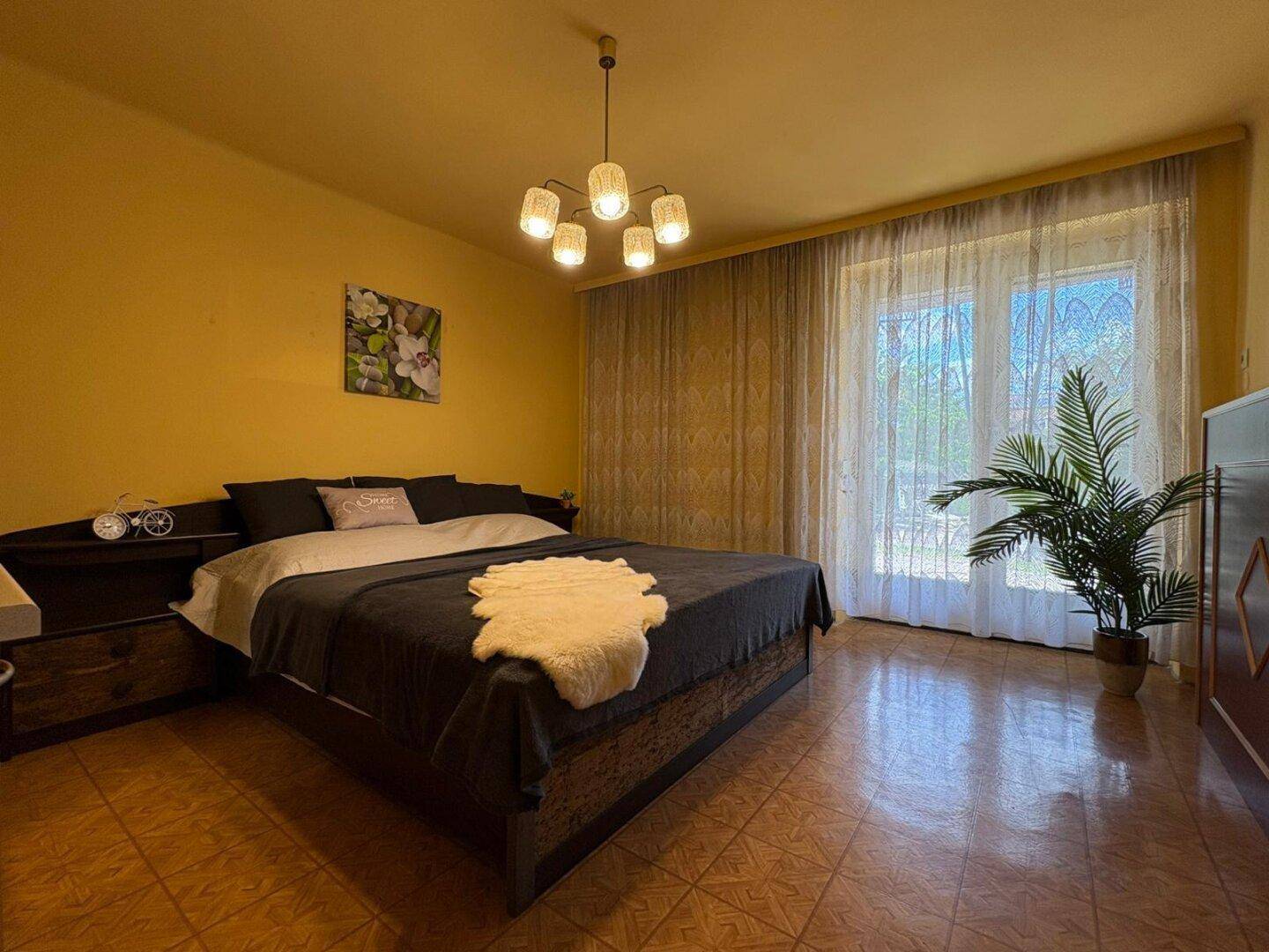 Großes Schlafzimmer mit Doppelbett, gelben Wänden und Fenster mit Vorhängen, bietet viel Licht.