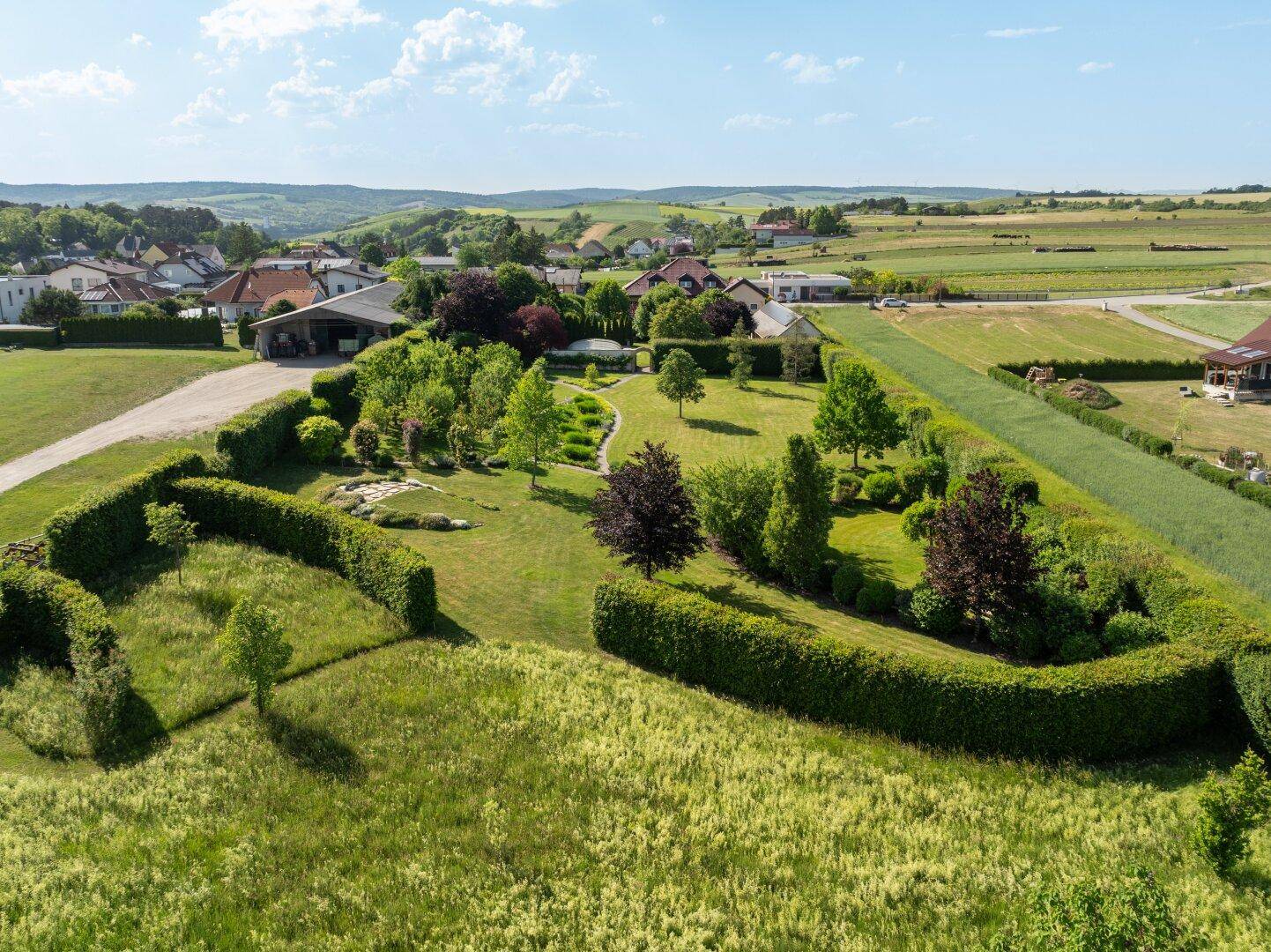 Luftaufnahme eines weitläufigen Anwesens mit gepflegten Hecken, Rasenflächen und einem Haus in ländlicher Umgebung.