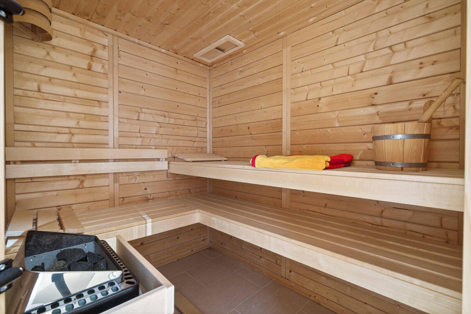 Moderne Holzsauna mit Bänken und Saunaofen für Entspannung und Wellness.