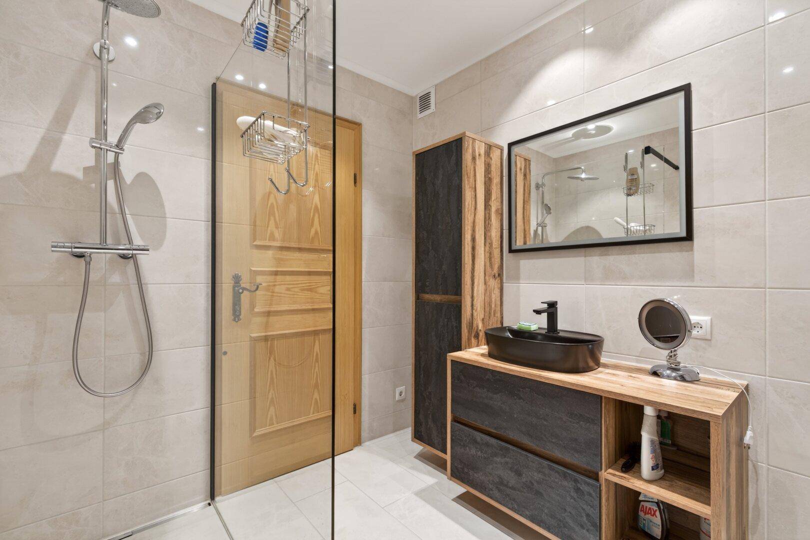 Modernes Badezimmer mit ebenerdiger Dusche, stilvollem Waschbecken und Holzmöbeln.