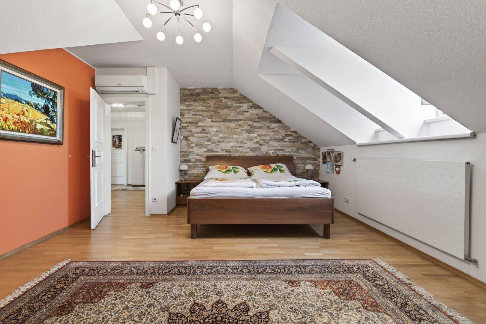 Gemütliches Schlafzimmer im Dachgeschoss mit Holzbett, Steinwand und Dachfenstern.