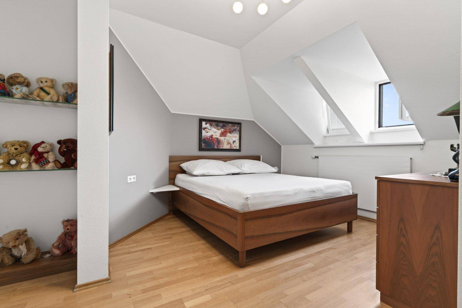 Helles Schlafzimmer im Dachgeschoss mit Holzbett, Dachfenstern und Holzboden.