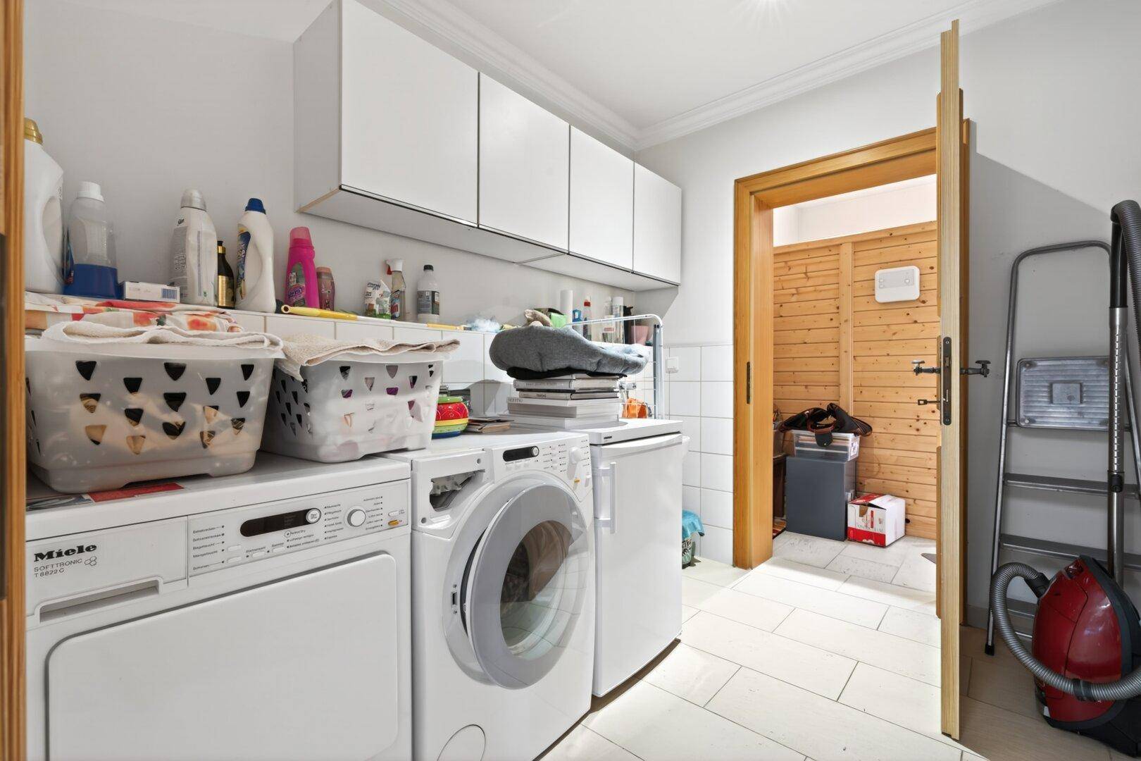 Funktionaler Hauswirtschaftsraum mit Waschmaschine, Trockner und Zugang zu einer holzvertäfelten Sauna.