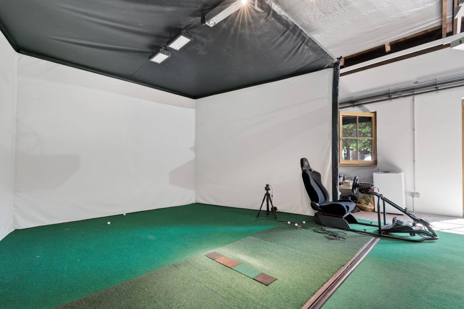 Spielzimmer mit Rennsimulator, grünem Teppichboden und einem Fenster für natürliches Licht.