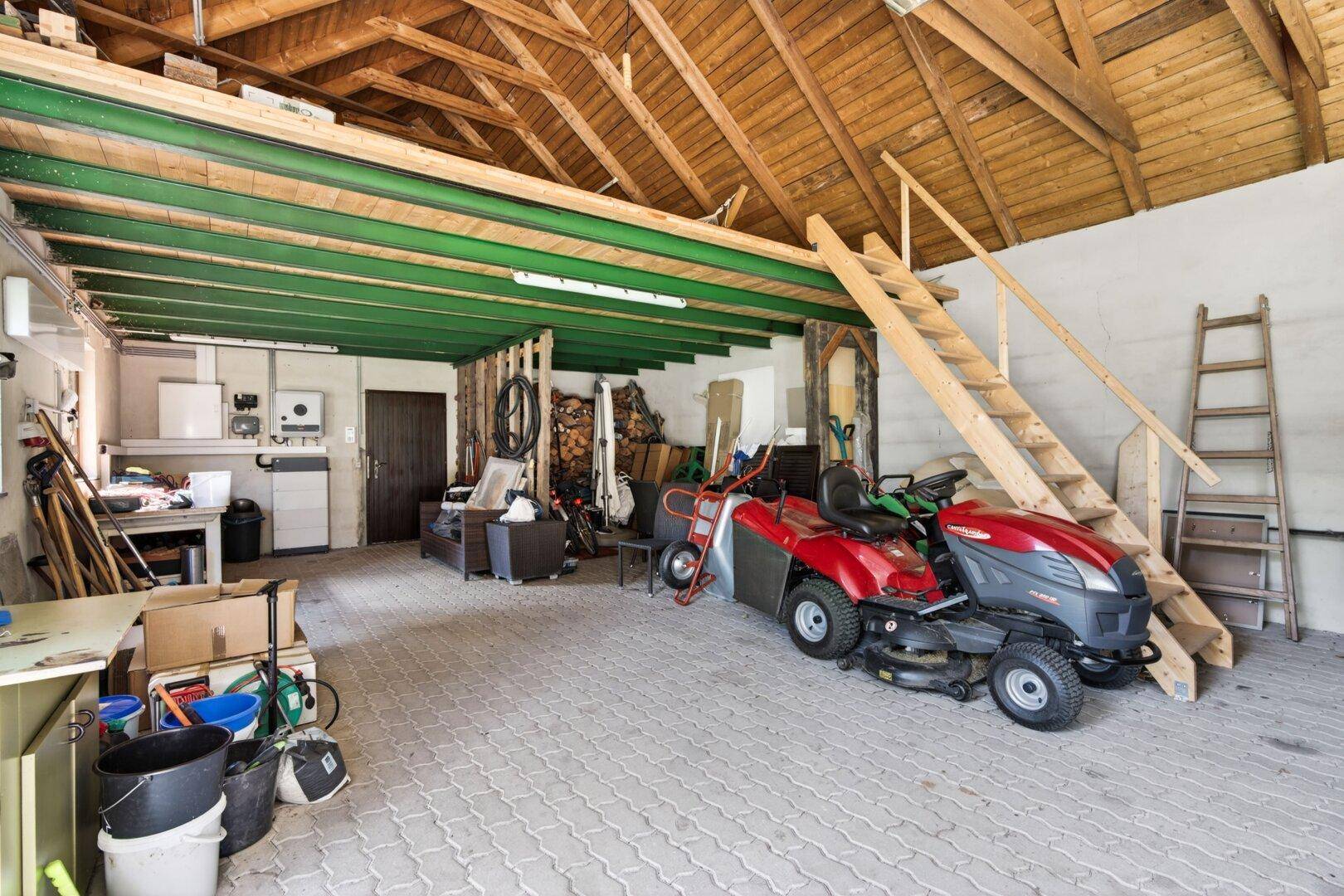 Geräumige Garage mit offenem Holzdachstuhl, Aufsitzrasenmäher und vielseitiger Lagerfläche.