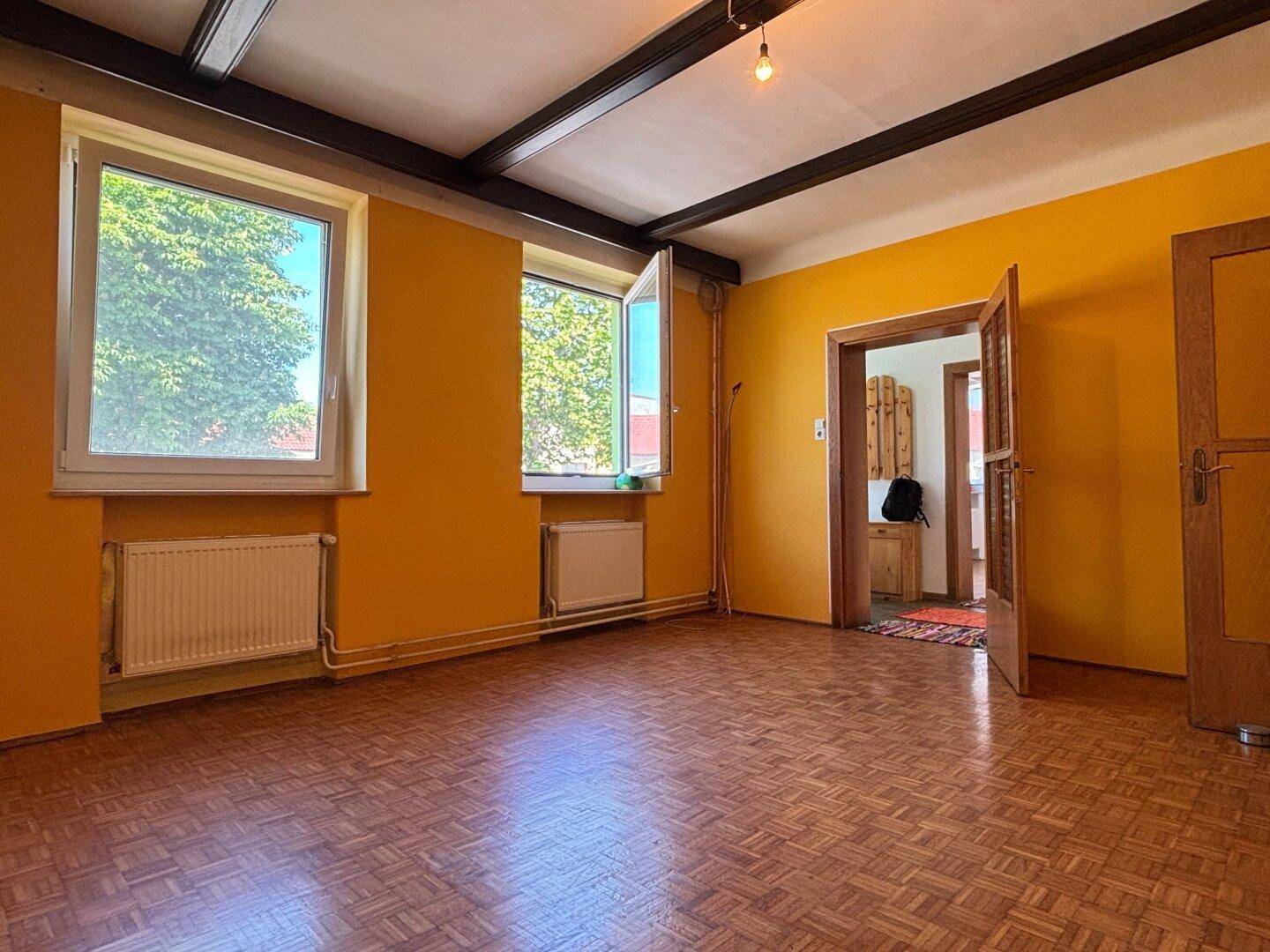 Helles Zimmer mit gelben Wänden, sichtbaren Holzbalken und klassischem Parkettboden.