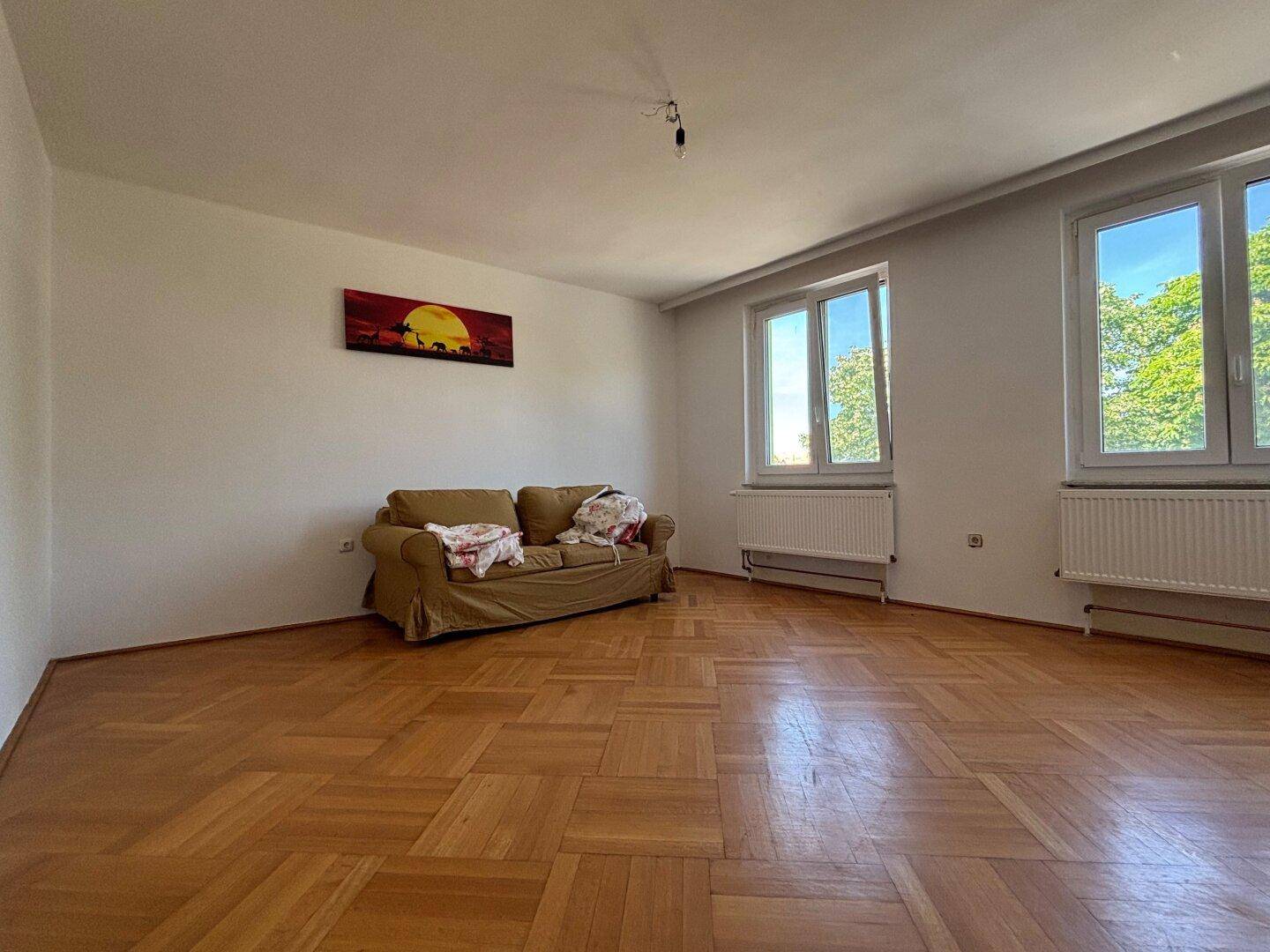 Großes Wohnzimmer mit Parkettboden, beigem Sofa und zwei hellen Fenstern.