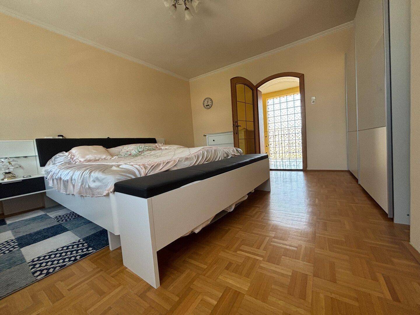Geräumiges Schlafzimmer mit Doppelbett, Kleiderschrank und klassischem Parkettboden.