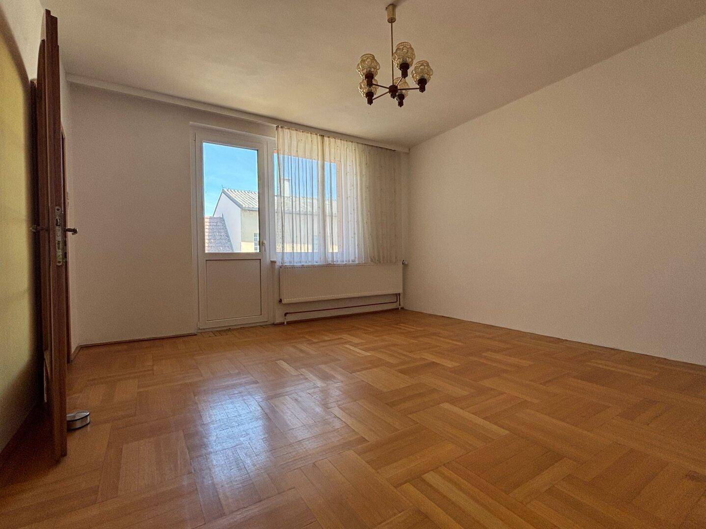 Helles Zimmer mit Parkettboden und direktem Zugang zu einem Balkon oder einer Terrasse.