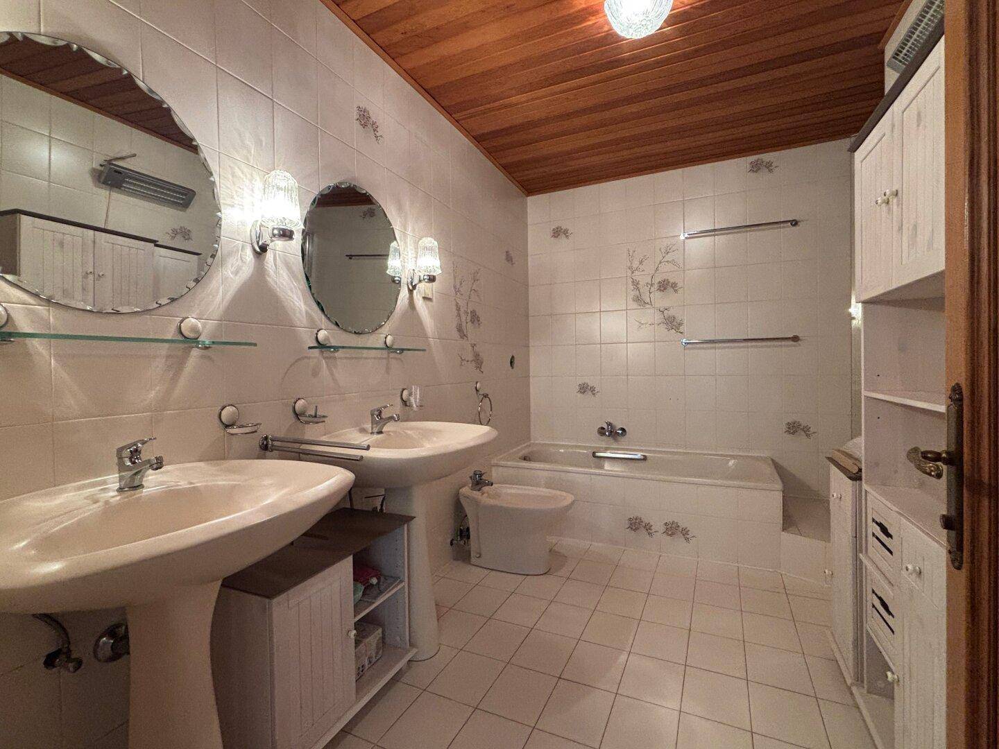 Klassisches Badezimmer mit zwei Waschbecken, Badewanne, Bidet und Holzdeckenverkleidung.
