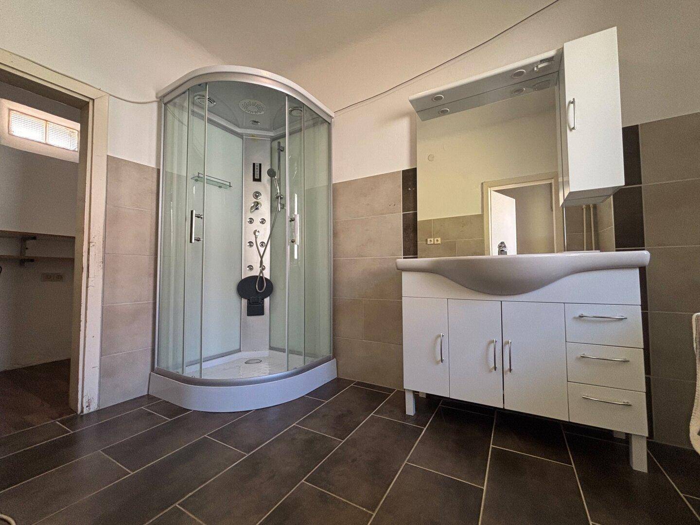 Modernes Badezimmer mit großer Duschkabine, elegantem Waschtisch und dunklen Bodenfliesen.