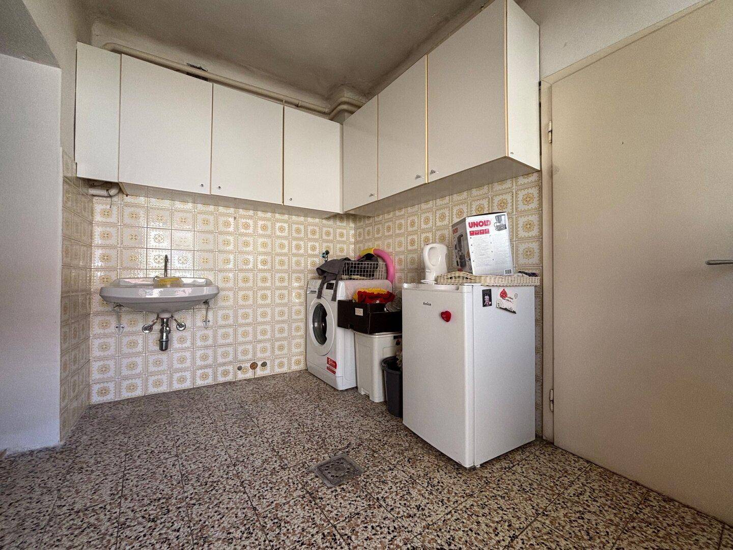 Praktischer Hauswirtschaftsraum mit Waschmaschine, Spülbecken und Stauraum in Oberschränken.