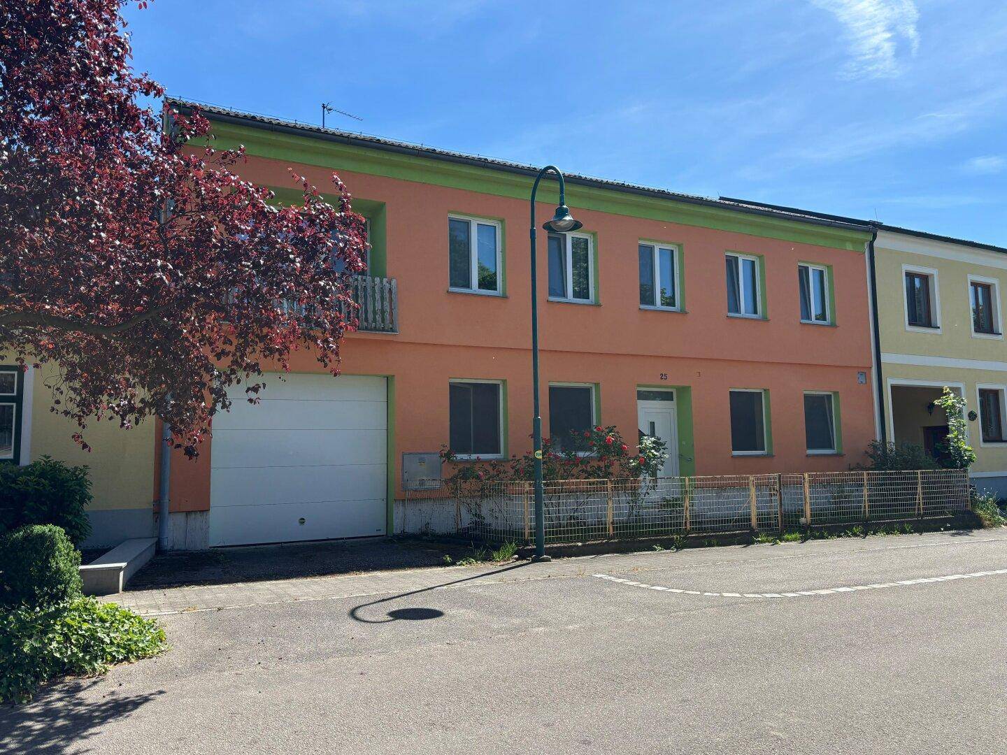 Fassade eines Wohnhauses in leuchtendem Orange mit grünen Akzenten und integrierter Garage.