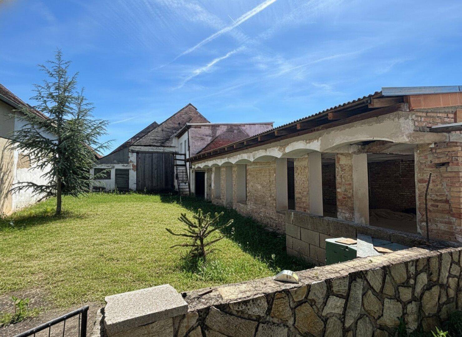 Großer Gartenbereich mit Rasenfläche, jungen Bäumen und angrenzendem alten Nebengebäude.