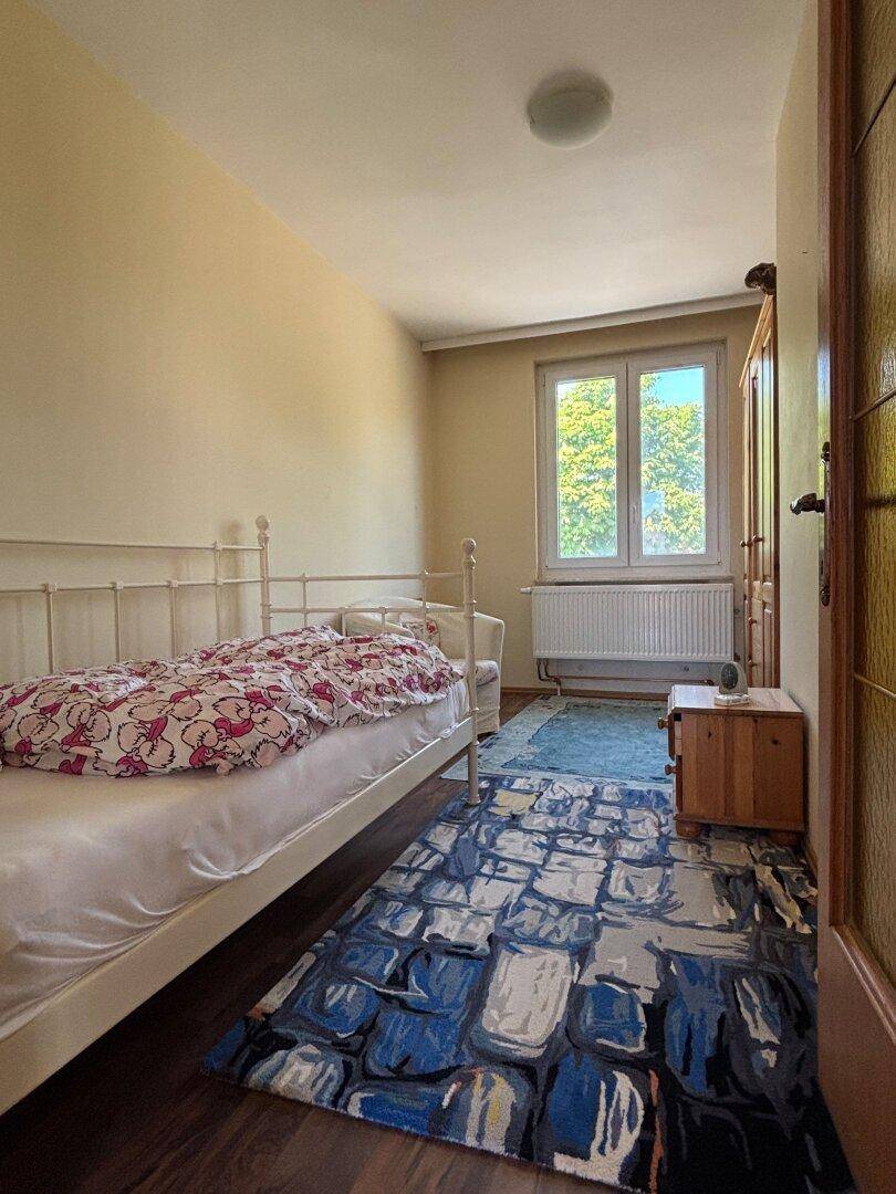 Helles Schlafzimmer mit Einzelbett, Holzschrank und einem Fenster mit Blick ins Grüne.