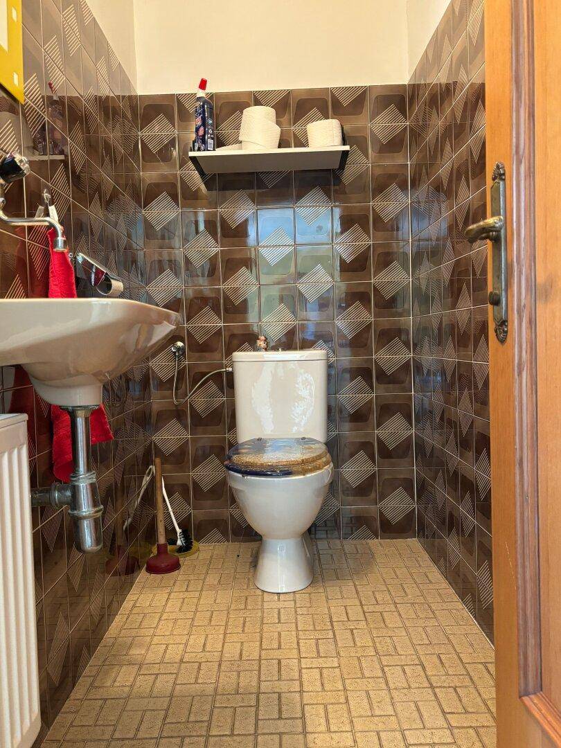 Kleines Gäste-WC mit Toilette und Waschbecken, komplett gefliest in Brauntönen.