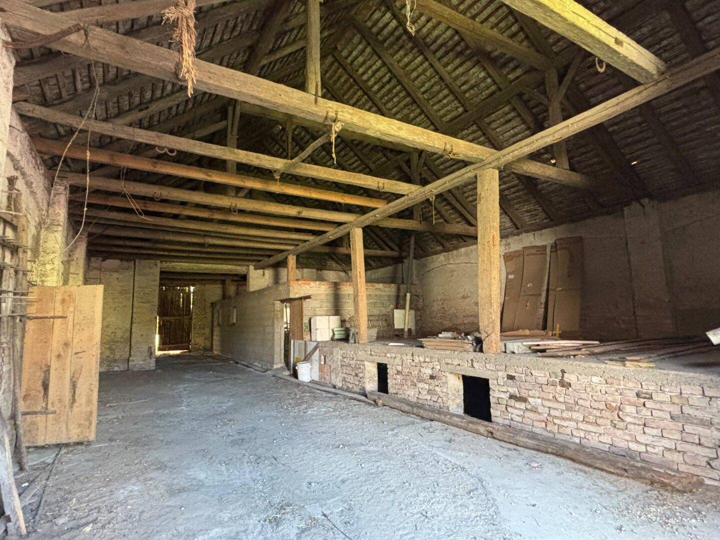 Geräumige Scheune mit sichtbarer Holzbalkenkonstruktion und rustikalen Ziegelwänden.