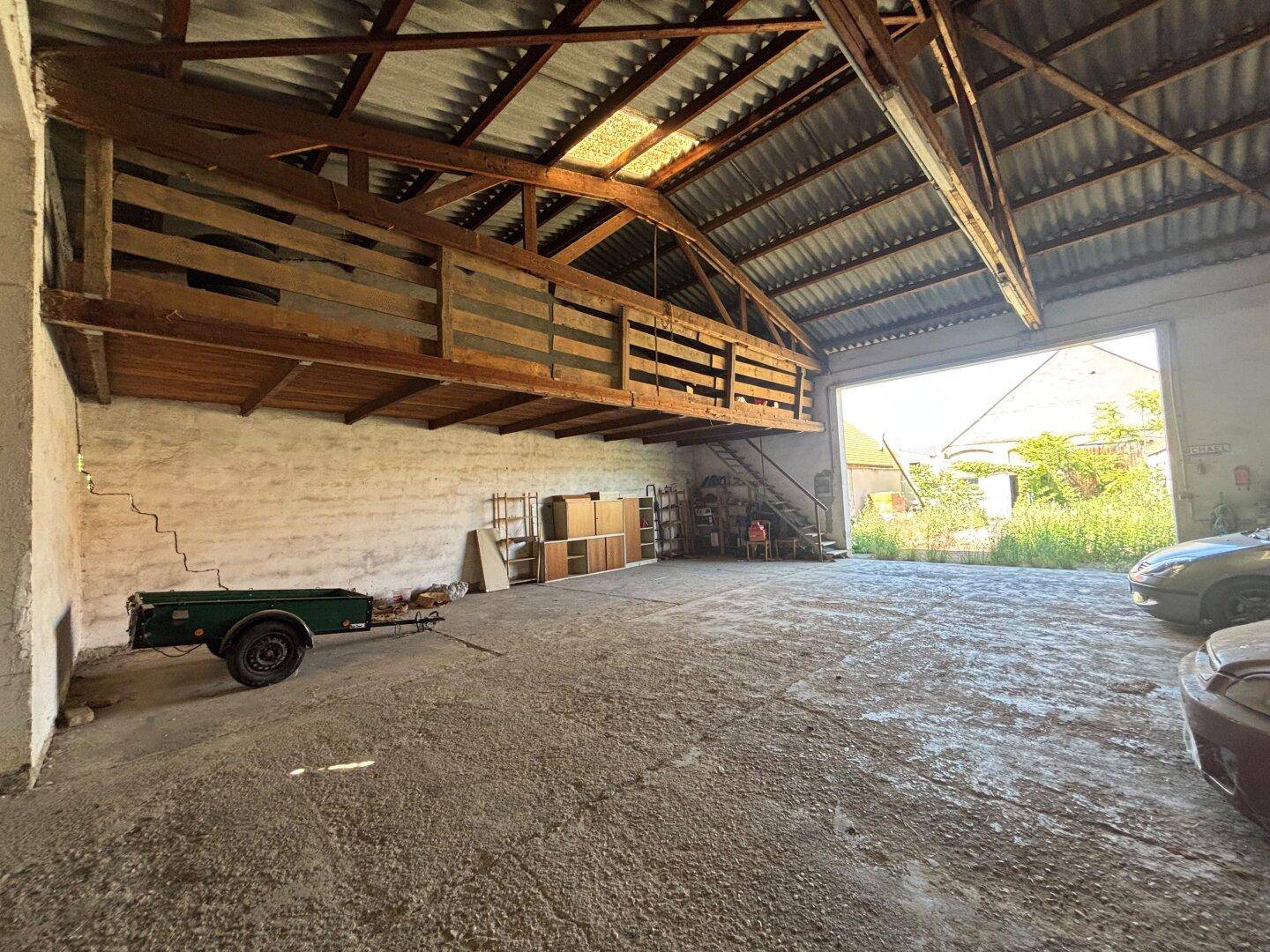 Große Garage oder Werkstatt mit hoher Decke und breitem Zugangstor für Fahrzeuge.