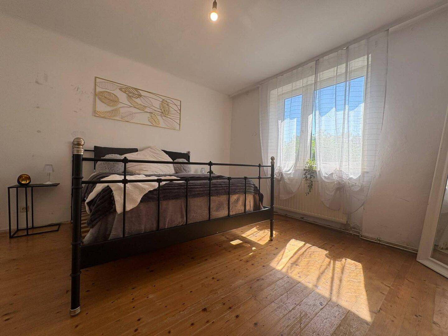 Schlafzimmer mit Holzdielenboden, Doppelbett und großen Fenstern für viel Licht.