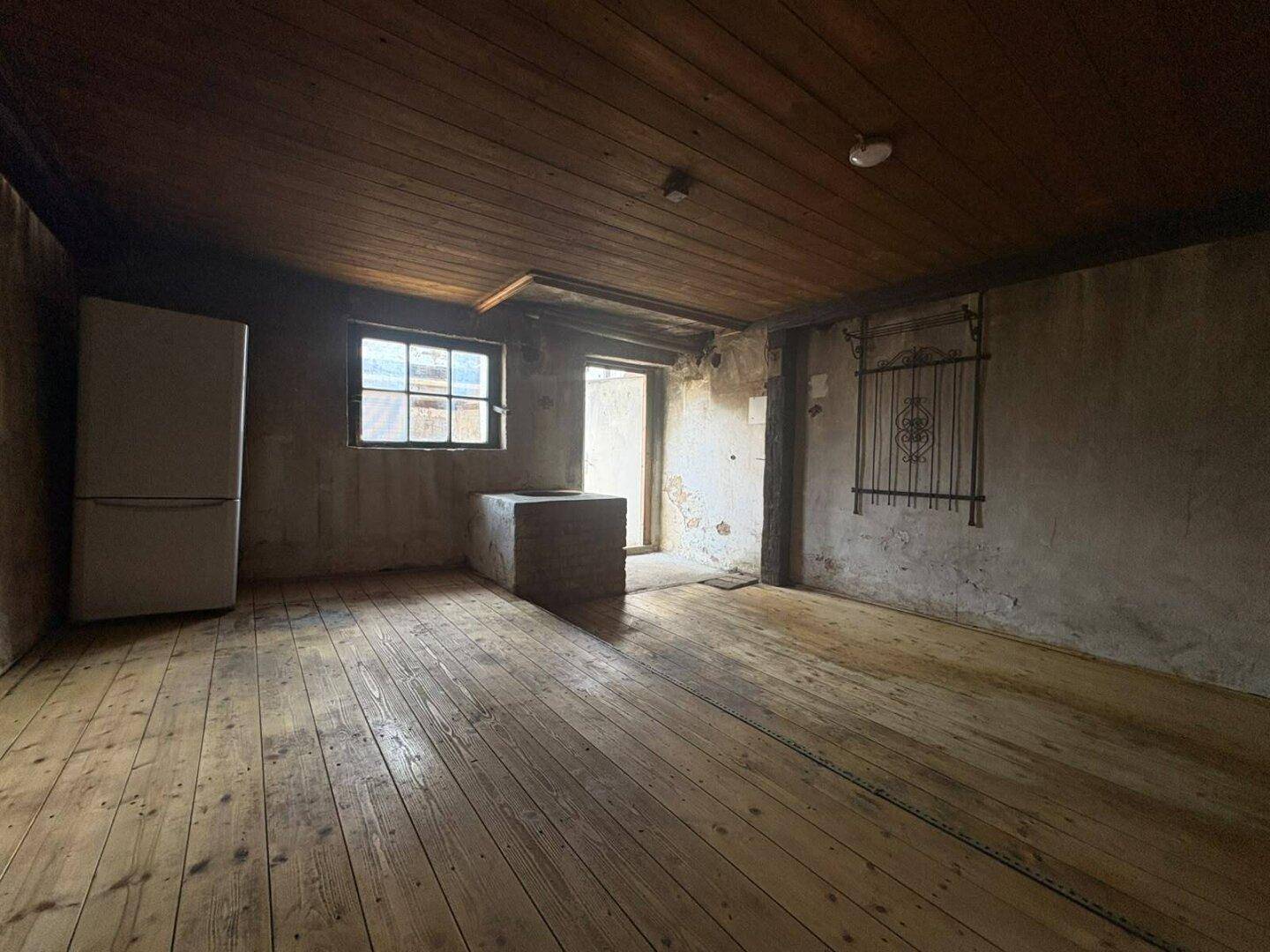 Rustikaler Kellerraum mit Holzdielenboden, Holzdecke und kleinem Fenster.