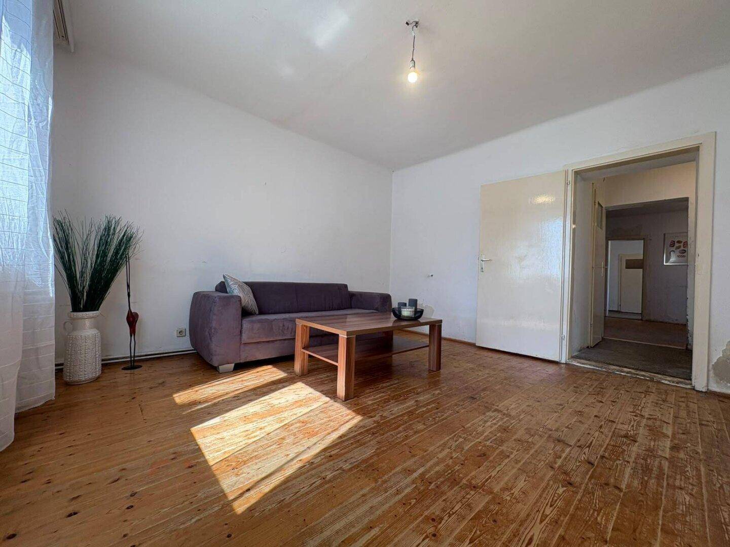 Geräumiges Wohnzimmer mit Holzdielenboden, Sofa und viel Tageslicht.