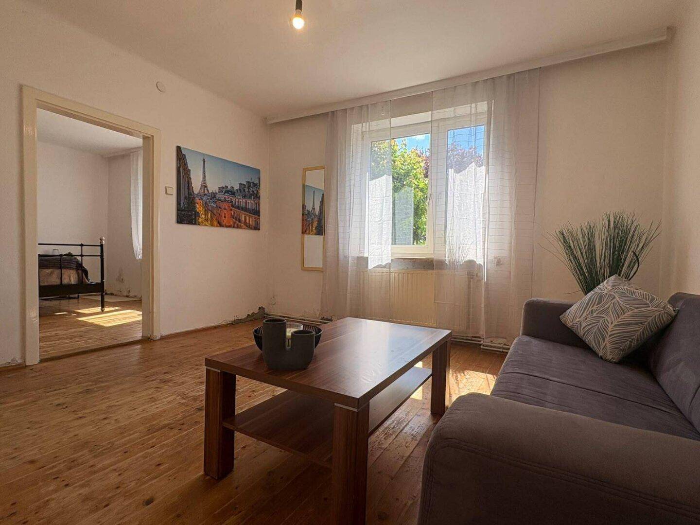 Helles Wohnzimmer mit Holzboden, Sofa und Blick ins Schlafzimmer.