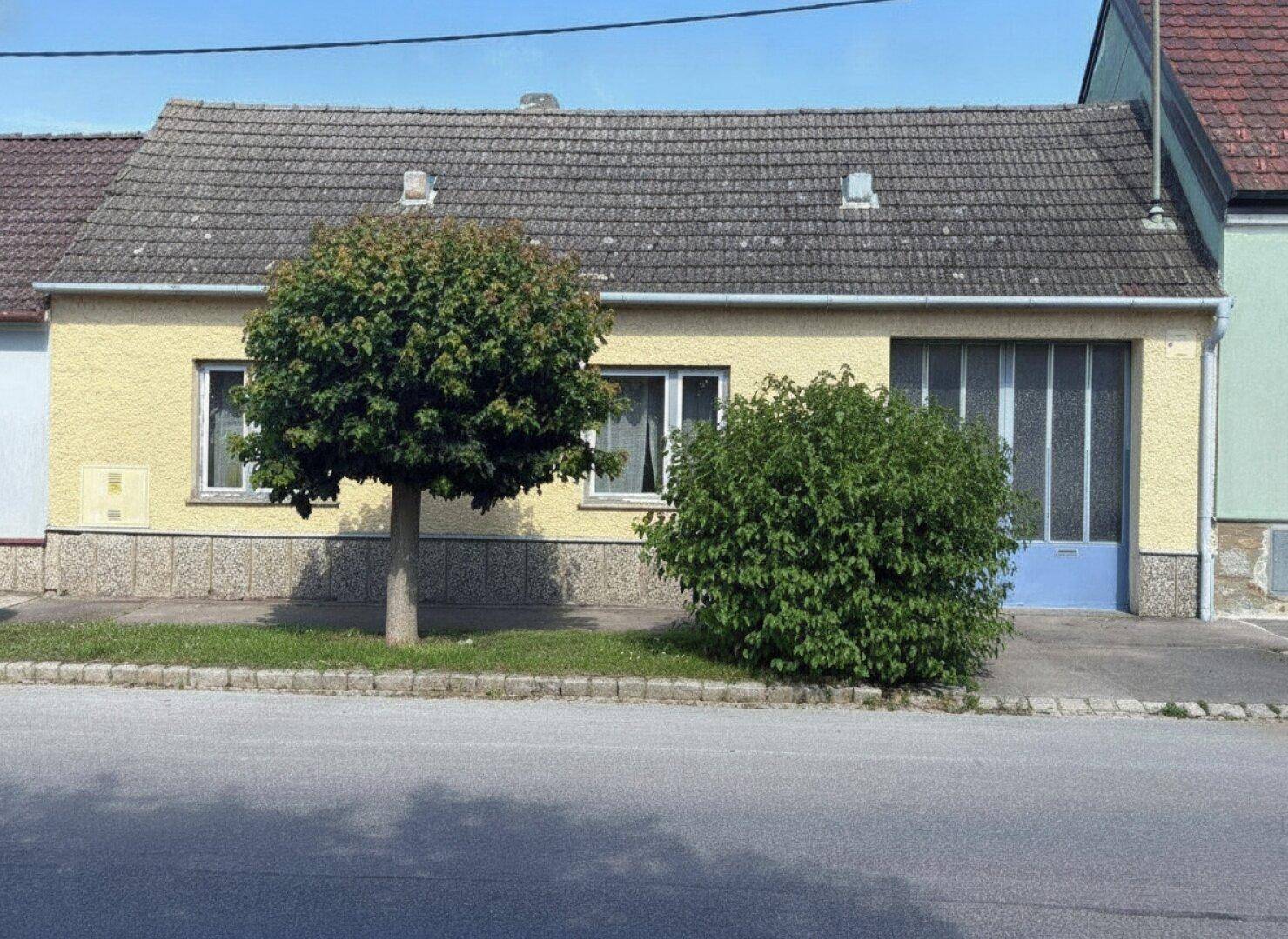 Gelbes Einfamilienhaus mit Satteldach und kleinen Fenstern an einer ruhigen Straße.