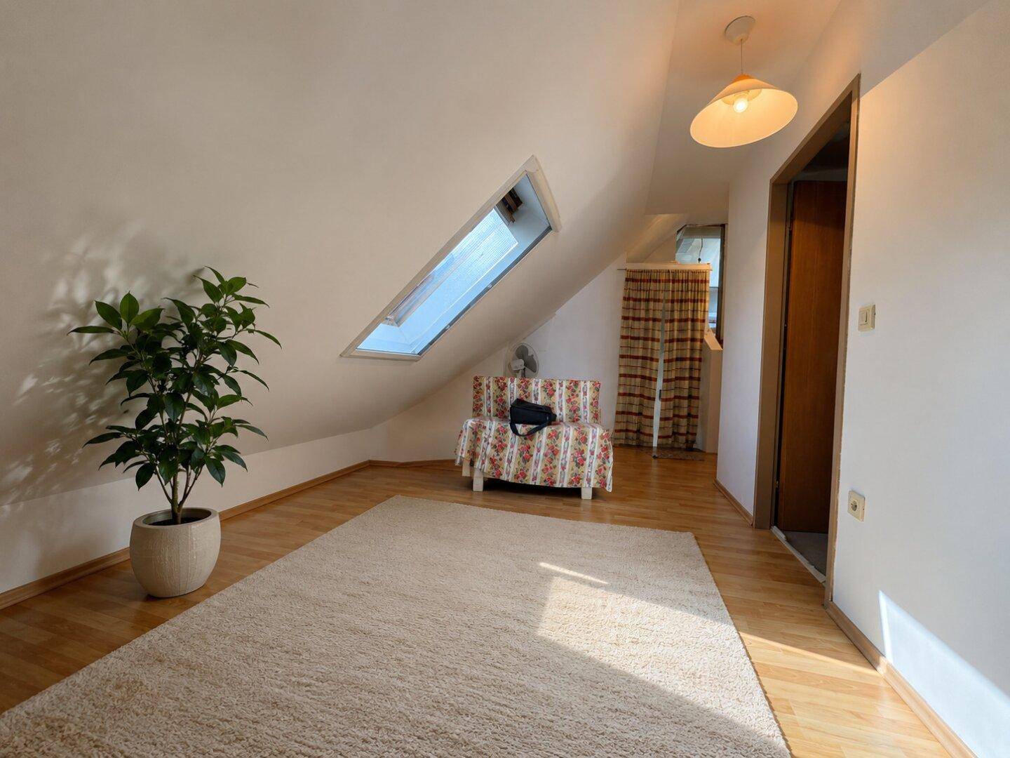 Helles Dachzimmer mit Holzboden, Teppich und Dachfenster, bietet vielseitige Nutzungsmöglichkeiten.