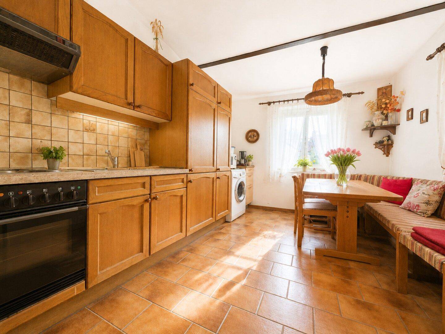 Traditionelle Holzküche mit Essbereich, Fliesenboden und Fenster, ausgestattet mit grundlegenden Geräten.