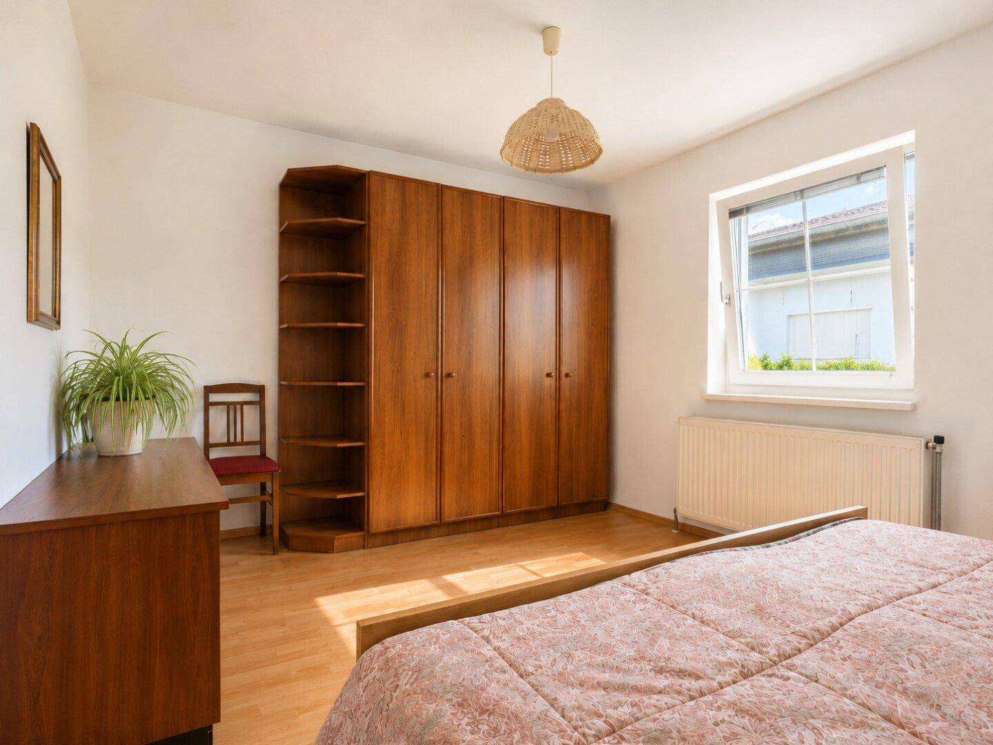 Schlafzimmer mit Holzschrank, Laminatboden und Fenster, einfach und funktional eingerichtet.