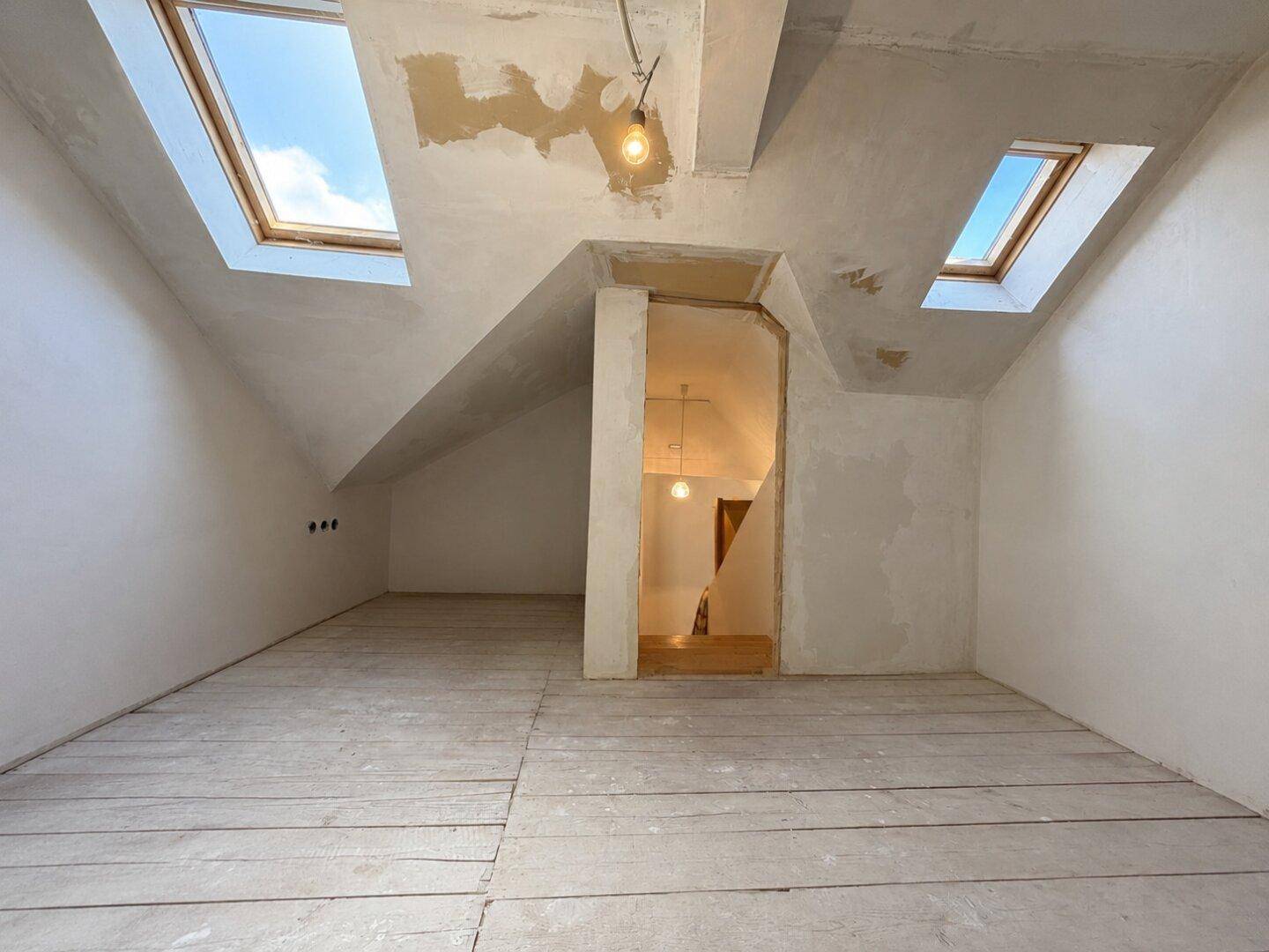 Dachbodenraum im Rohzustand mit Holzdielenboden und Dachfenstern, bereit für den Ausbau.