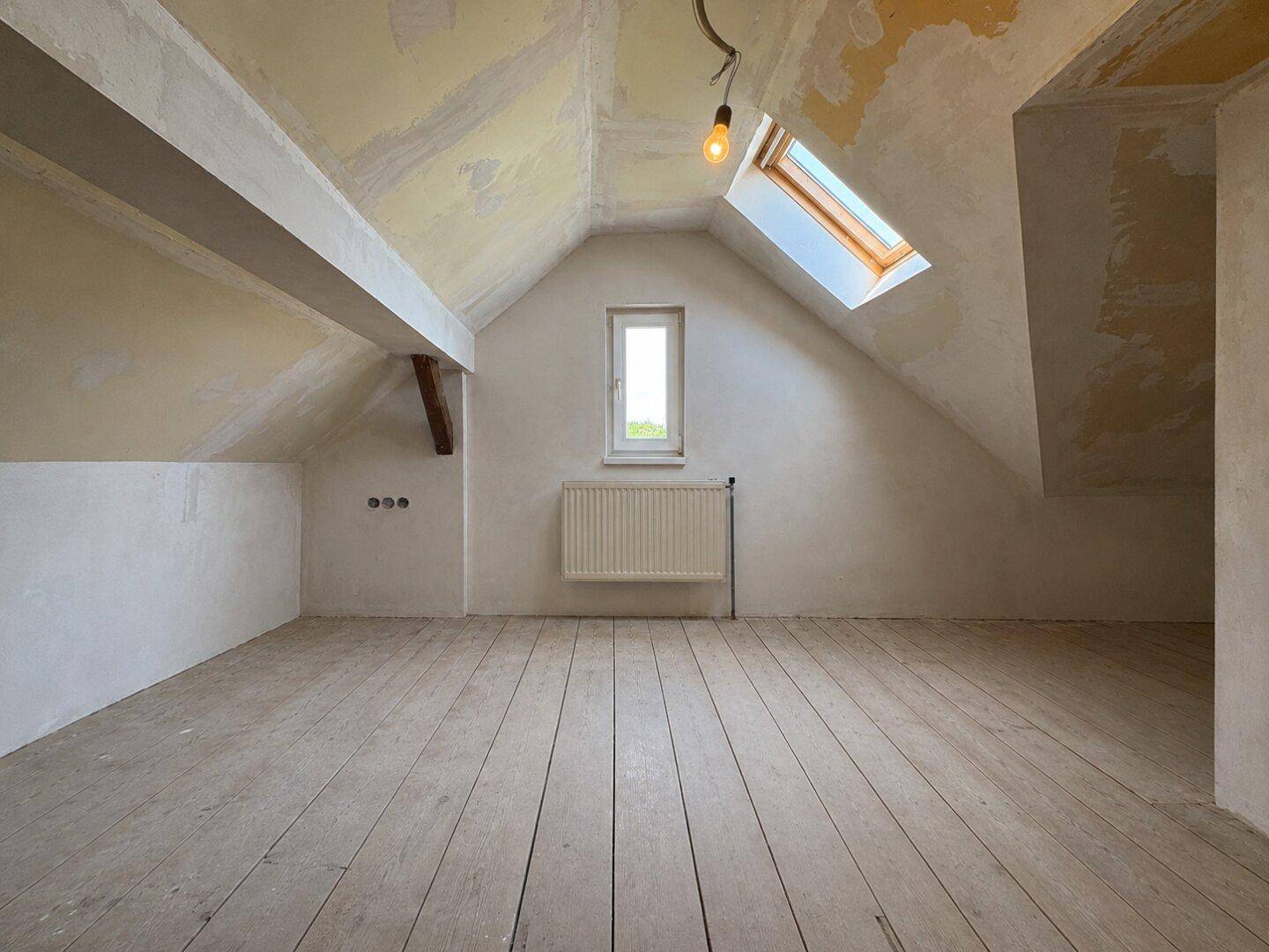 Dachbodenraum im Rohzustand mit Holzdielenboden und Dachfenster, bietet Ausbaupotenzial.