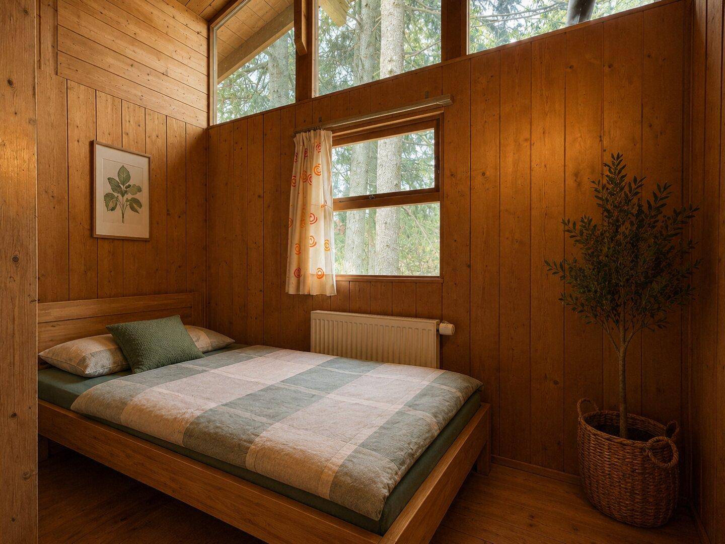 Schlafzimmer mit Holzbett, Holzvertäfelung und großen Fenstern mit Blick ins Grüne.