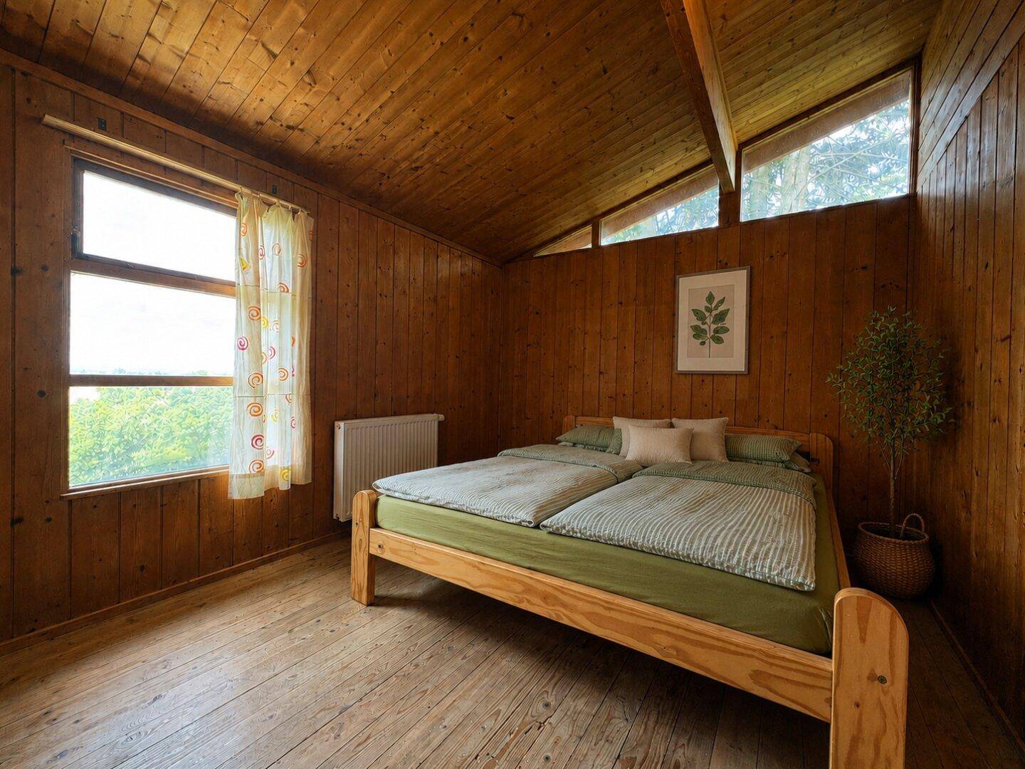 Schlafzimmer mit Doppelbett, Holzvertäfelung und schrägen Decken, hell durch große Fenster.