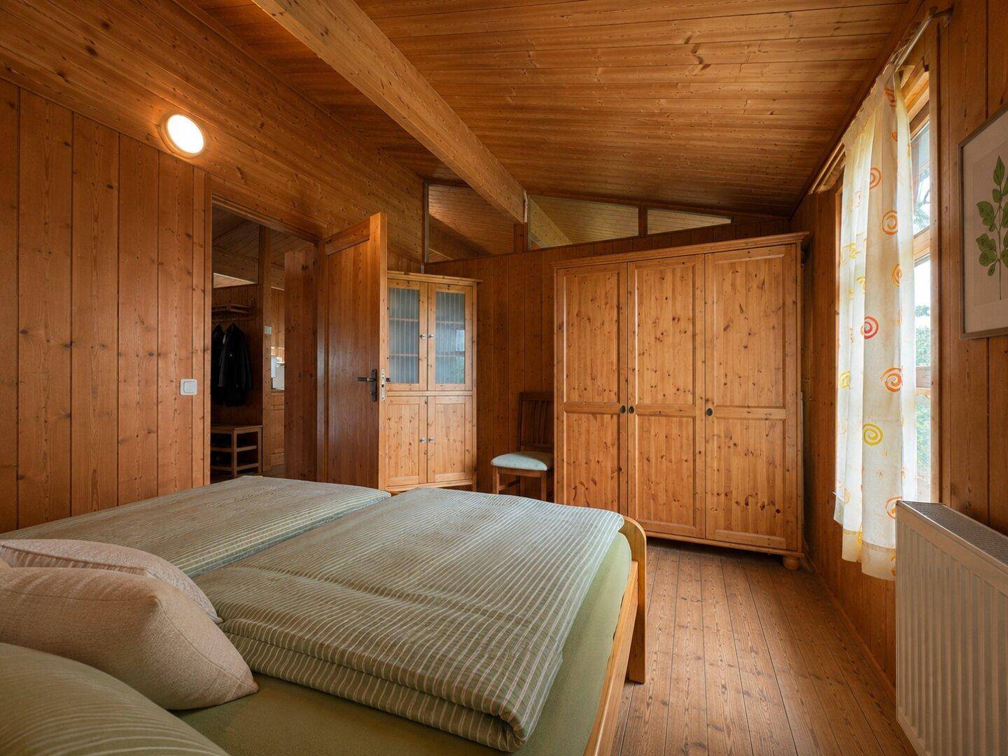 Schlafzimmer mit Doppelbett, Holzschränken und Zugang zu einem weiteren Raum.