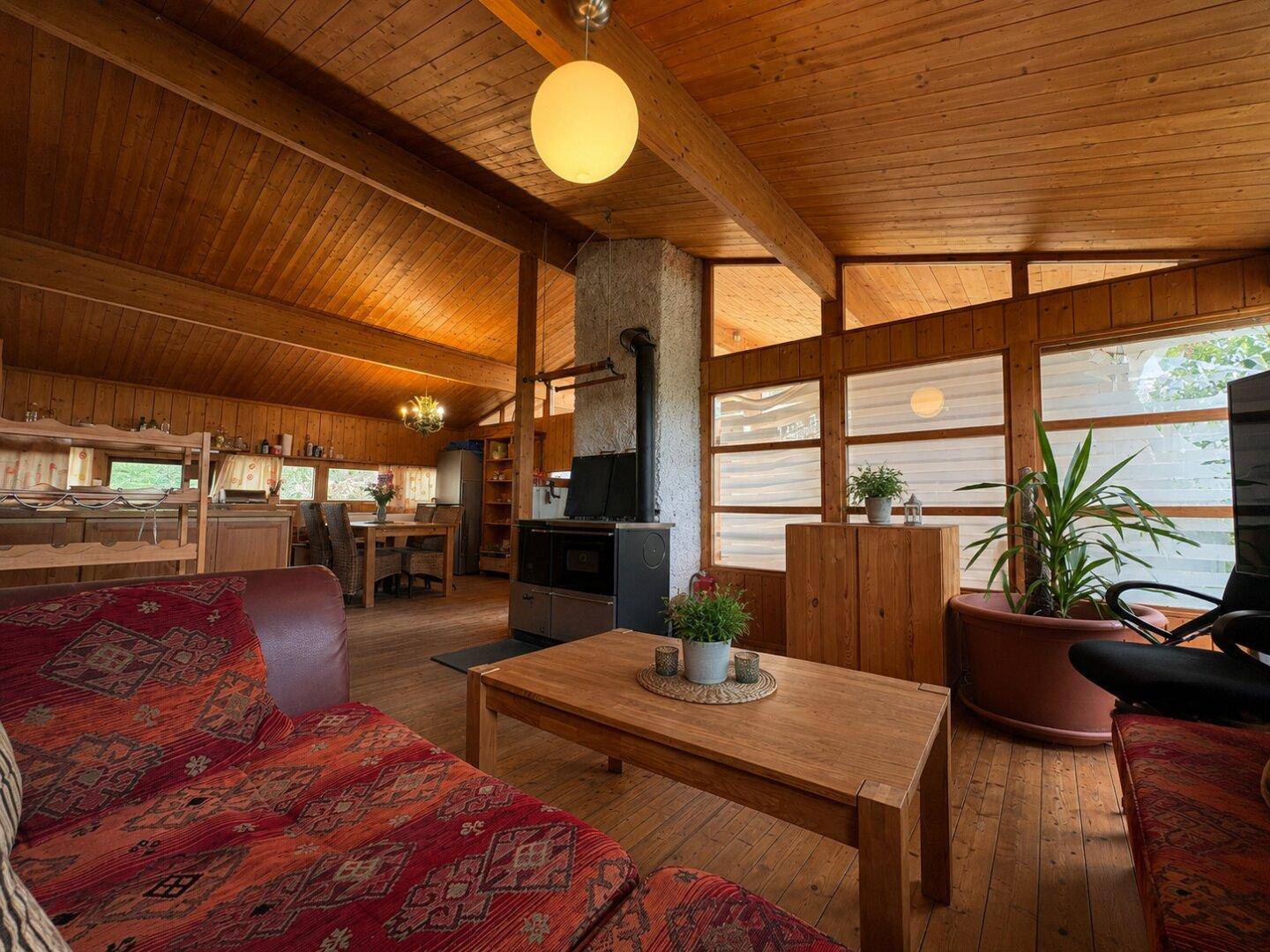 Geräumiges Wohnzimmer mit Holzbalkendecke, Kaminofen und großen Fenstern.