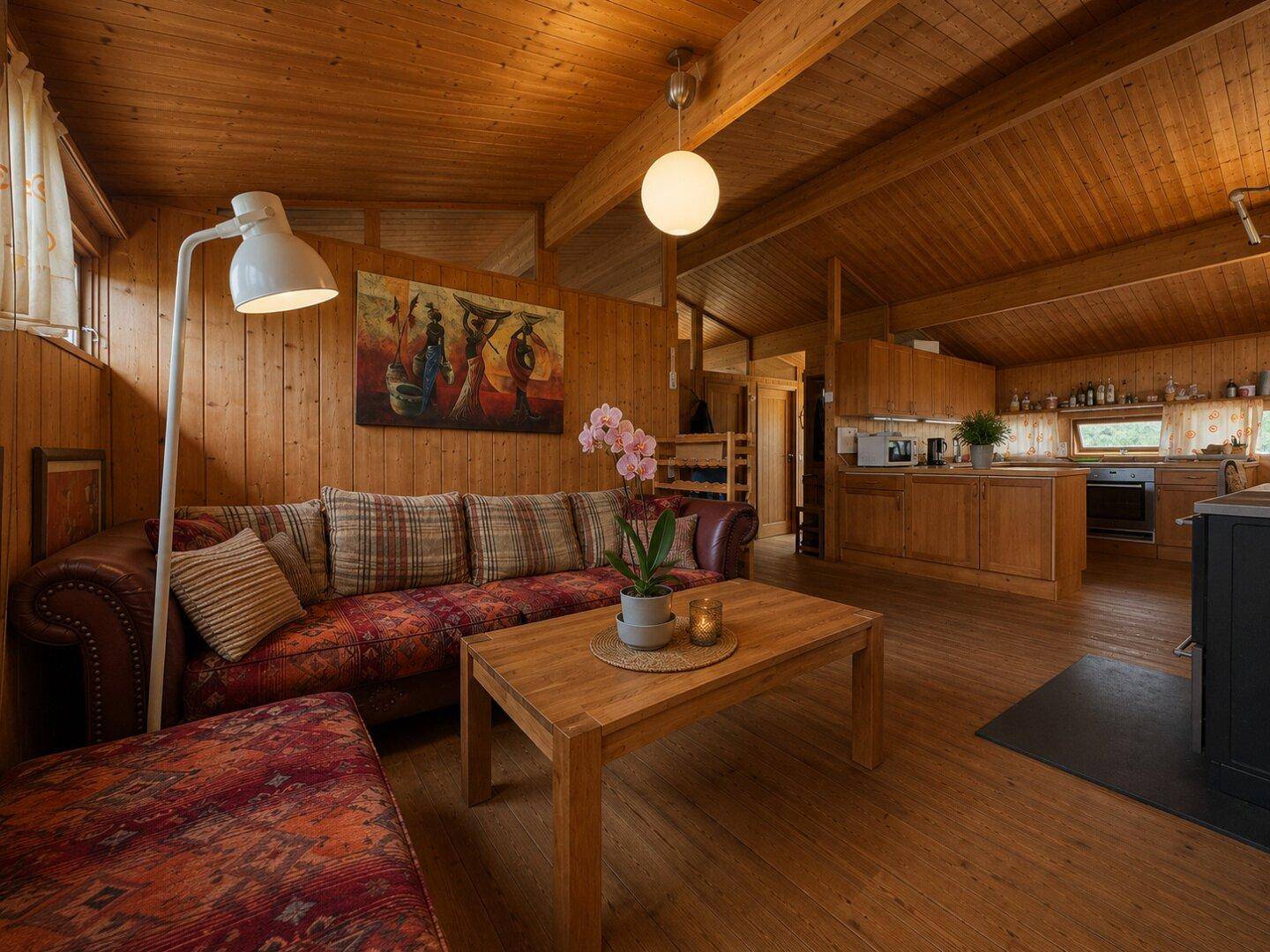 Offener Wohn- und Essbereich mit Holzbalkendecke, gemütlichem Sofa und integrierter Küche.